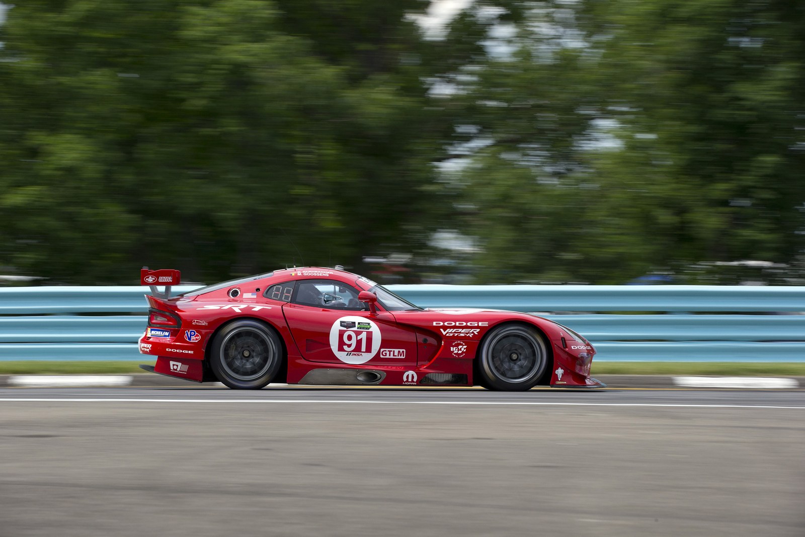 Red #91 GT race car at speed alongside a blue guardrail
