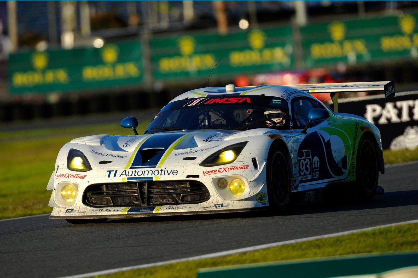 White and green #93 GT race car cornering with headlights on